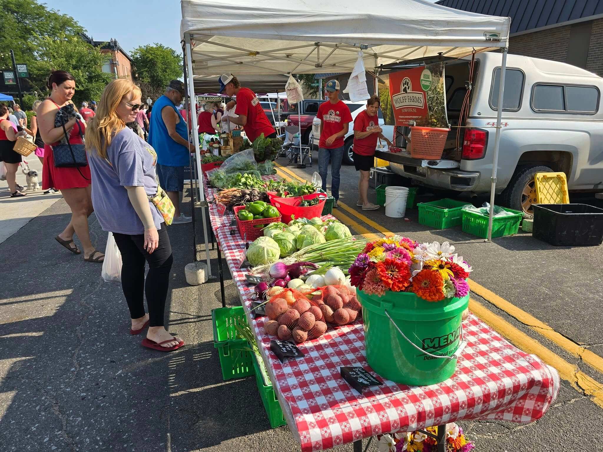 People standing by a Norfolk Farmers Market booth full of produce and flowers